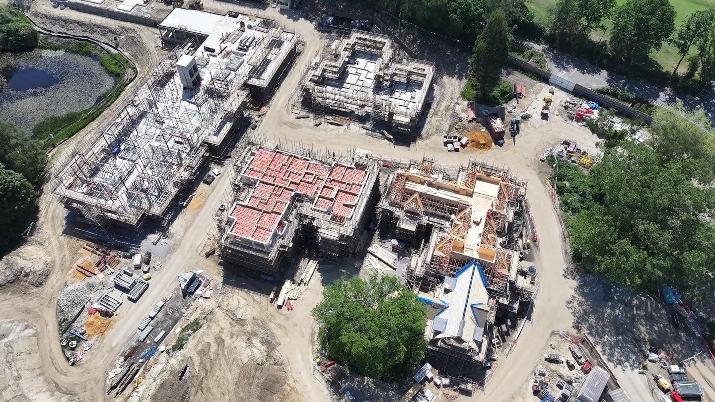 Top-down aerial view of a housing development under construction, showing several blocks with exposed concrete floors, scaffolding and partially built roofs.