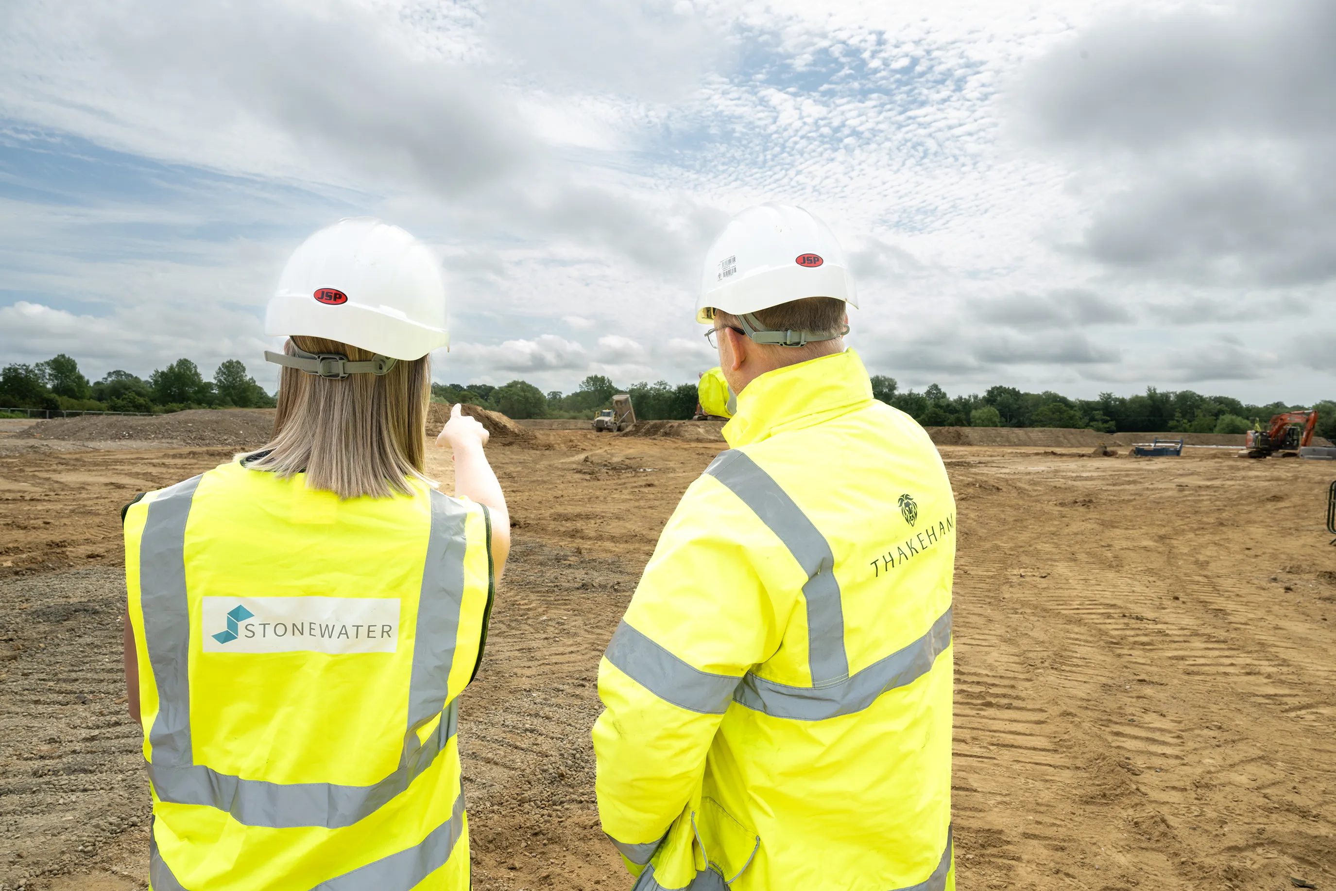 Two people in hard hats and hi-vis vests looking over a construction site, one pointing into the distance