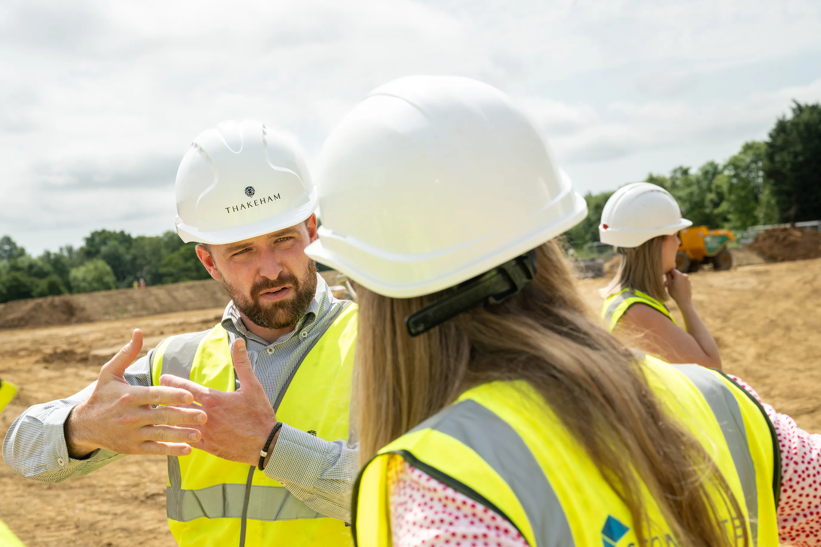 People in hard hats and hi-vis vests talking on a construction site, one gesturing with hands