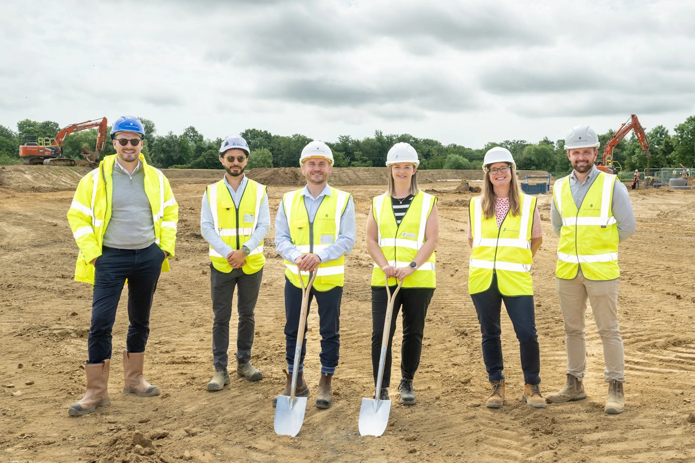 Group of workers in hard hats and hi-vis vests standing on a construction site with shovels