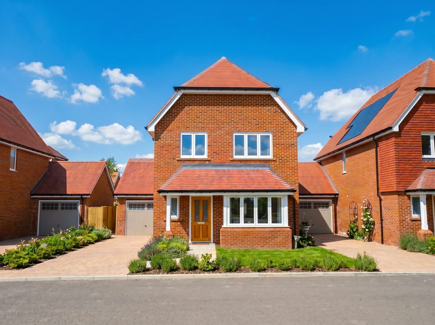 Detached red brick house with garage, orange front door, and solar panels on a new housing development.