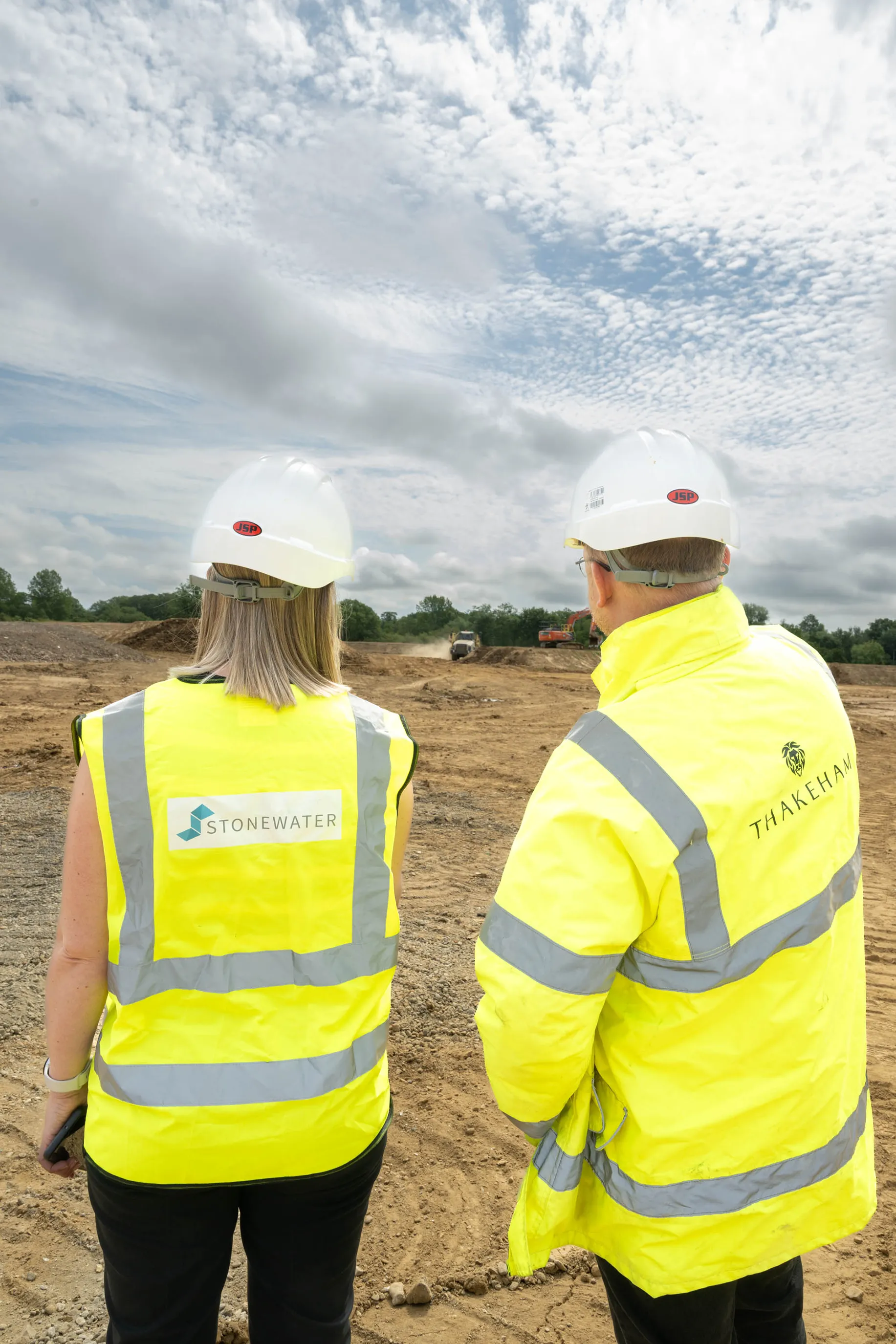 Two people in hard hats and hi-vis vests looking over a construction site, one pointing into the distance