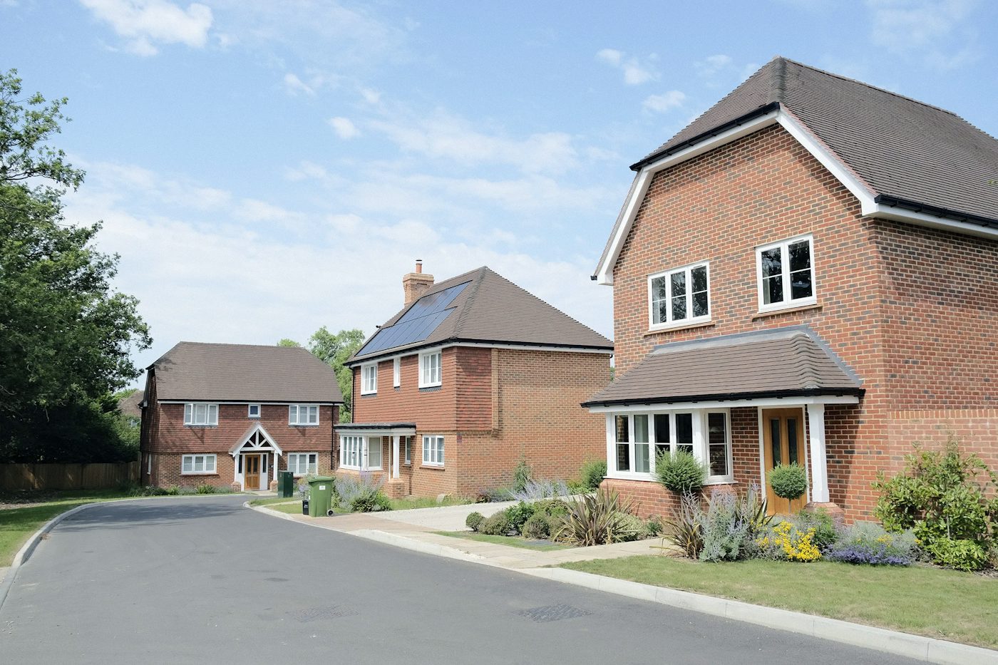 Row of new build brick houses in a suburban area, with planting and blue skies.