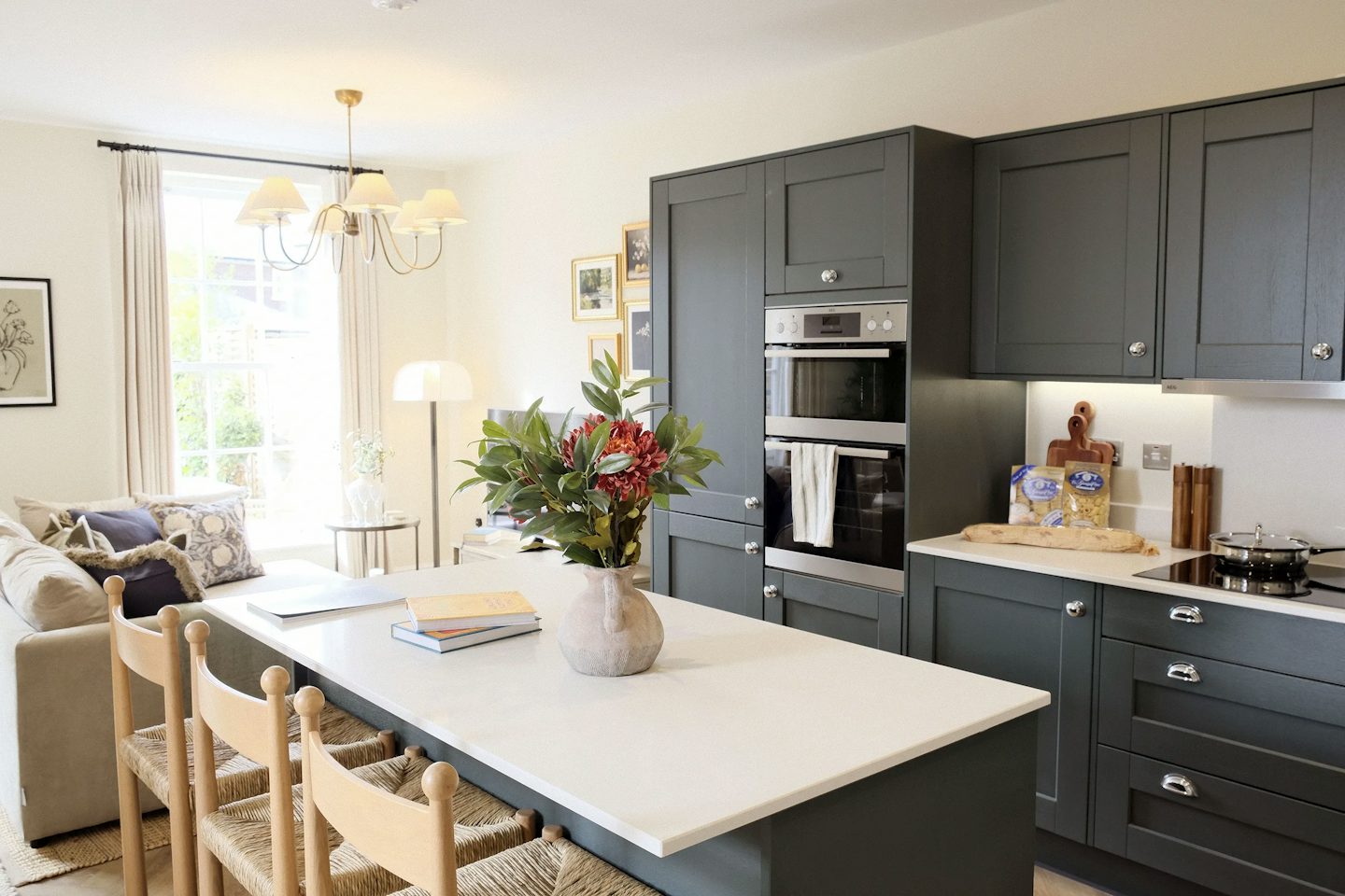 Open-plan kitchen and living space with a large island, dark cabinetry, pendant lighting, and a seating area by a bright window.