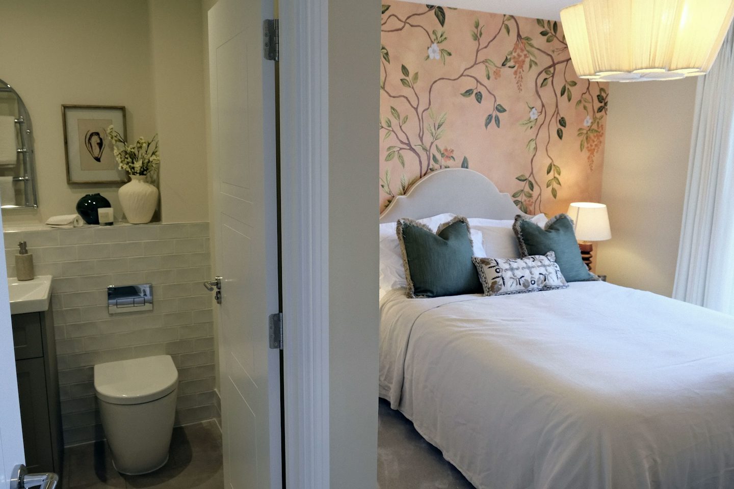 View from an en-suite bathroom into a stylish bedroom featuring floral wallpaper, a double bed with decorative cushions, and warm lighting.