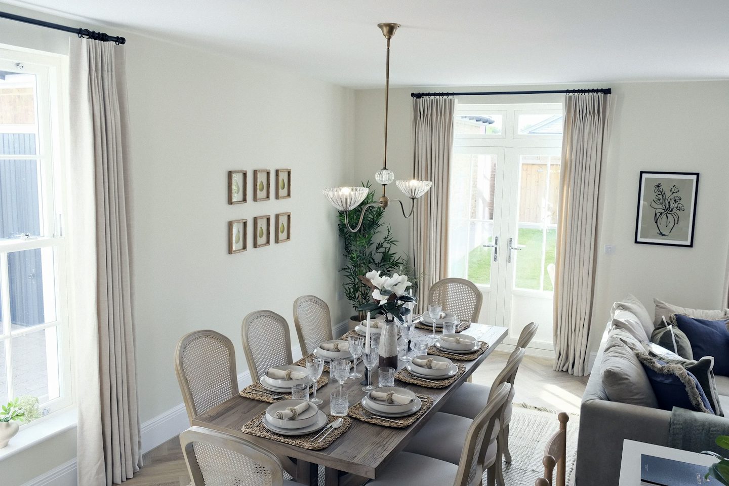 Open-plan dining and living area featuring a large dining table set for six, upholstered chairs, French doors to the garden, and a comfortable seating area with a sofa and decorative cushions.