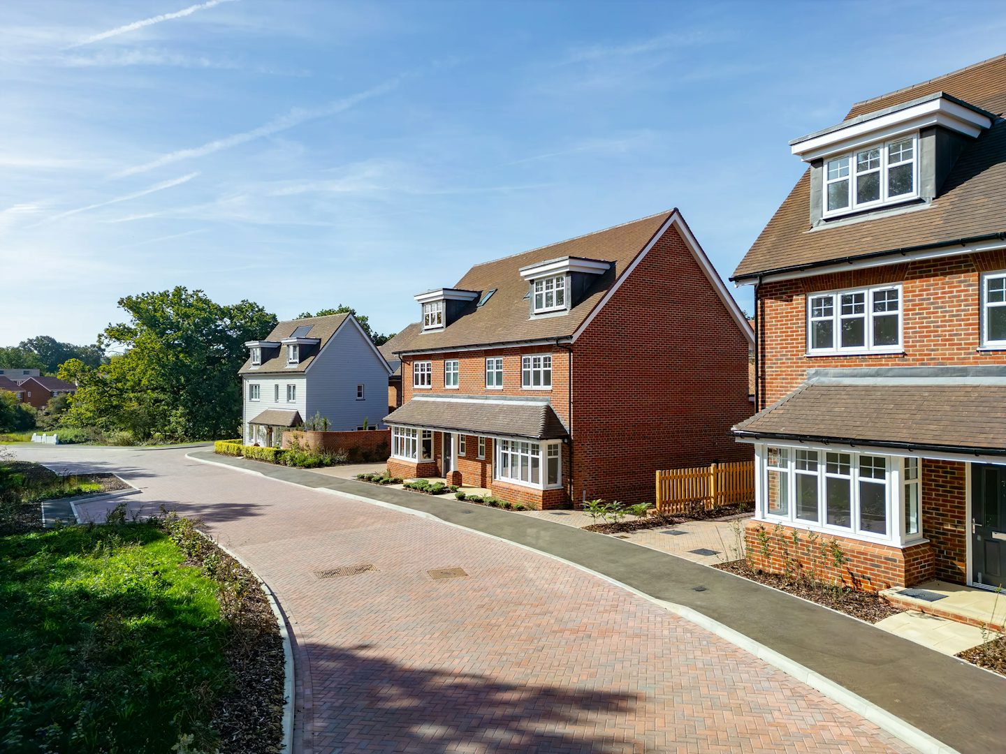 Residential street featuring newly built detached homes, landscaped front gardens, and a curved paved roadway.
