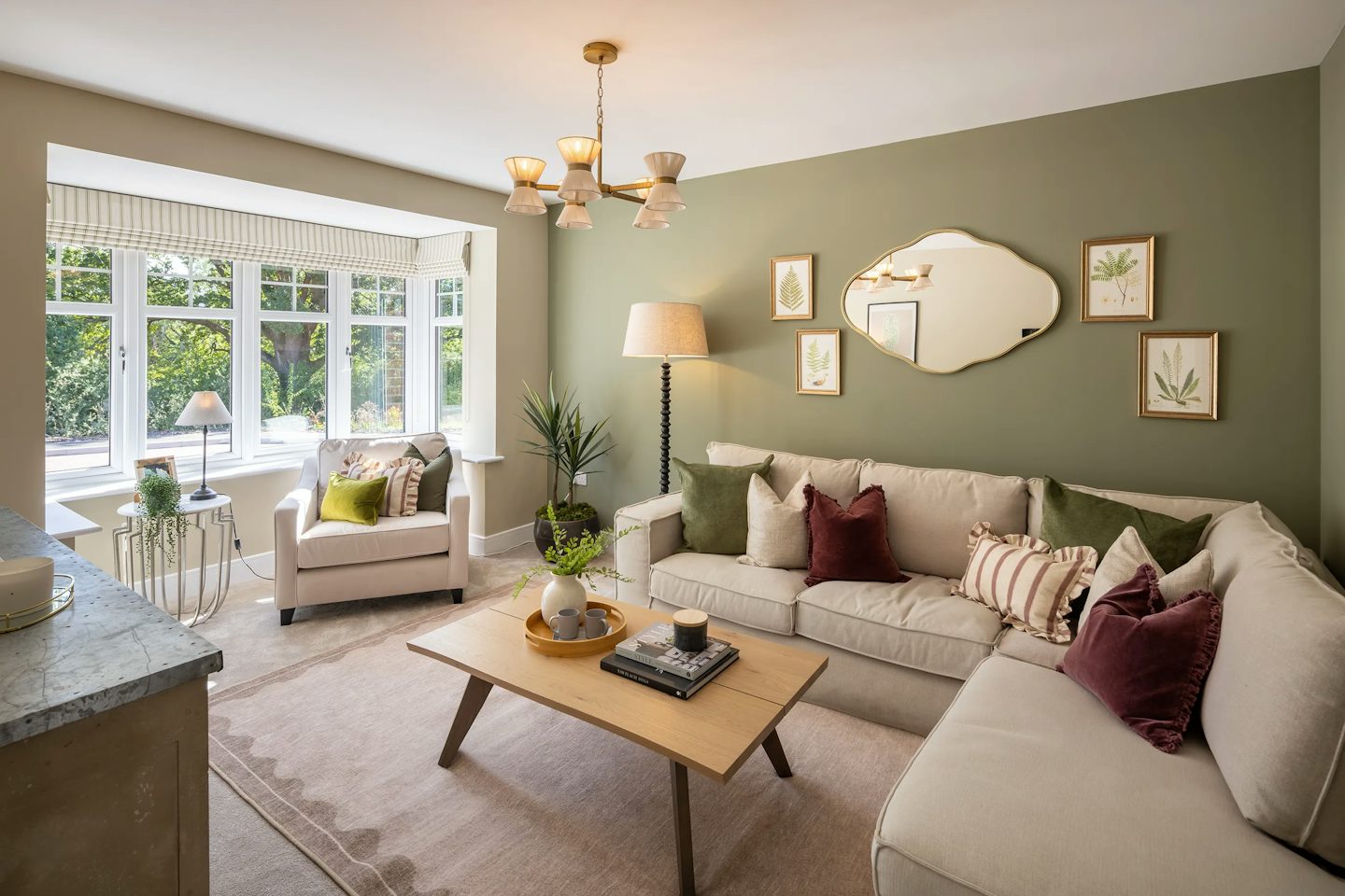 Contemporary living room with a large corner sofa, wooden coffee table, feature green wall, and bay window overlooking trees.