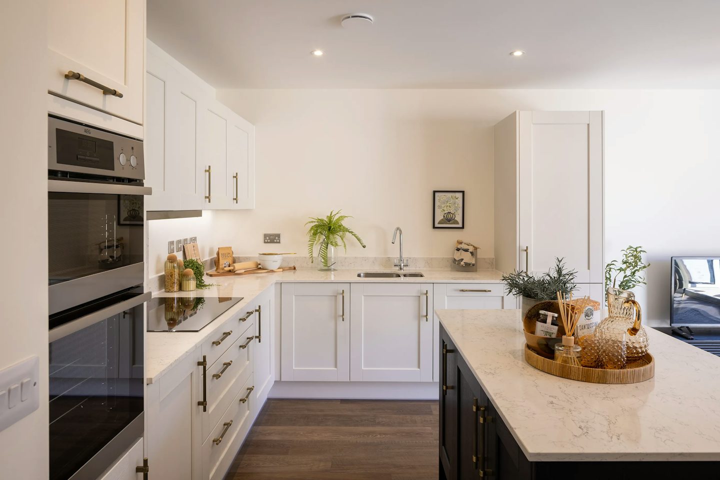Spacious open-plan kitchen with a large island breakfast bar, white cabinetry, integrated appliances, and wood-effect flooring.