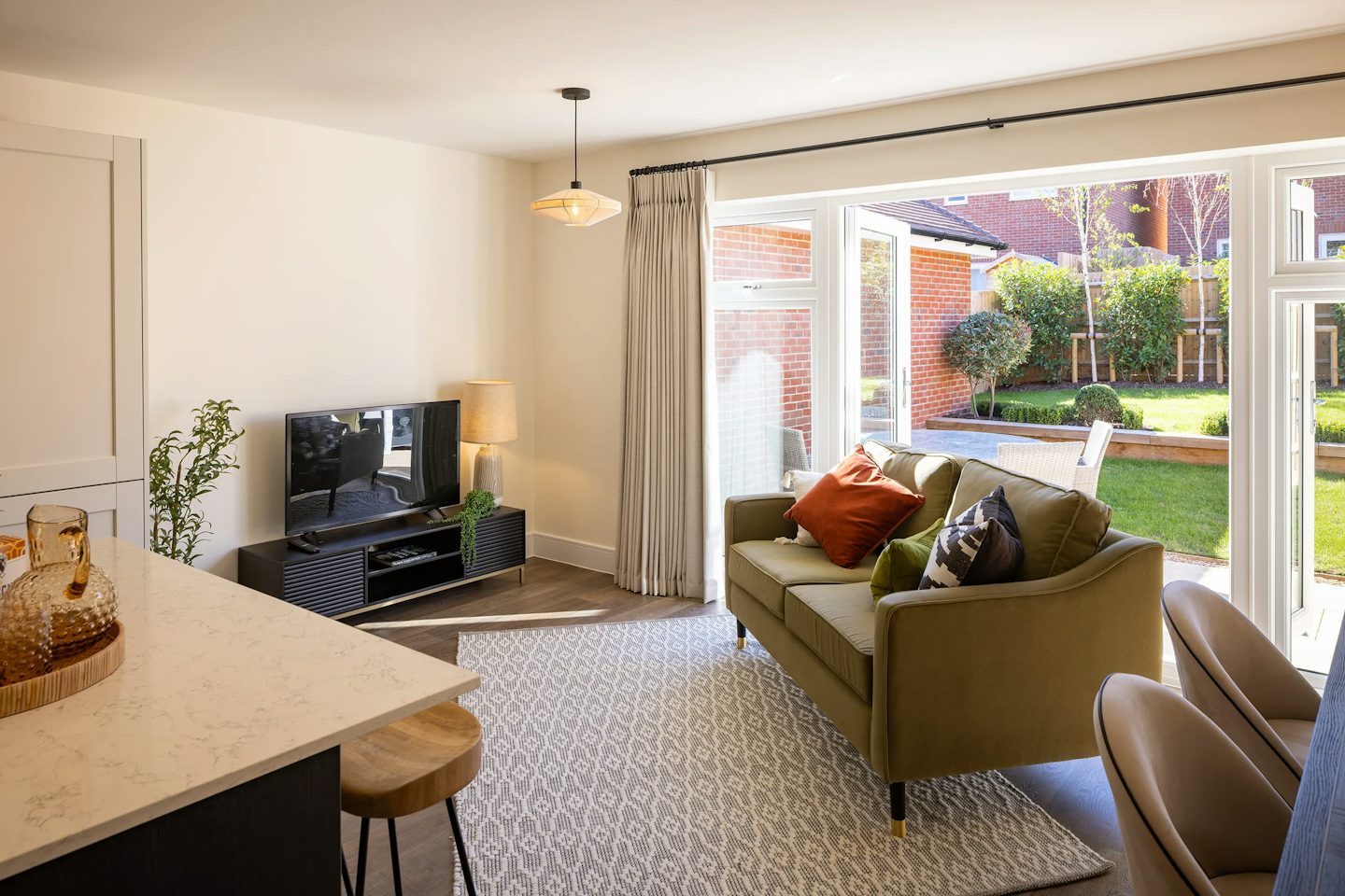 Bright living room with a sofa, television, and French doors opening onto a landscaped rear garden.