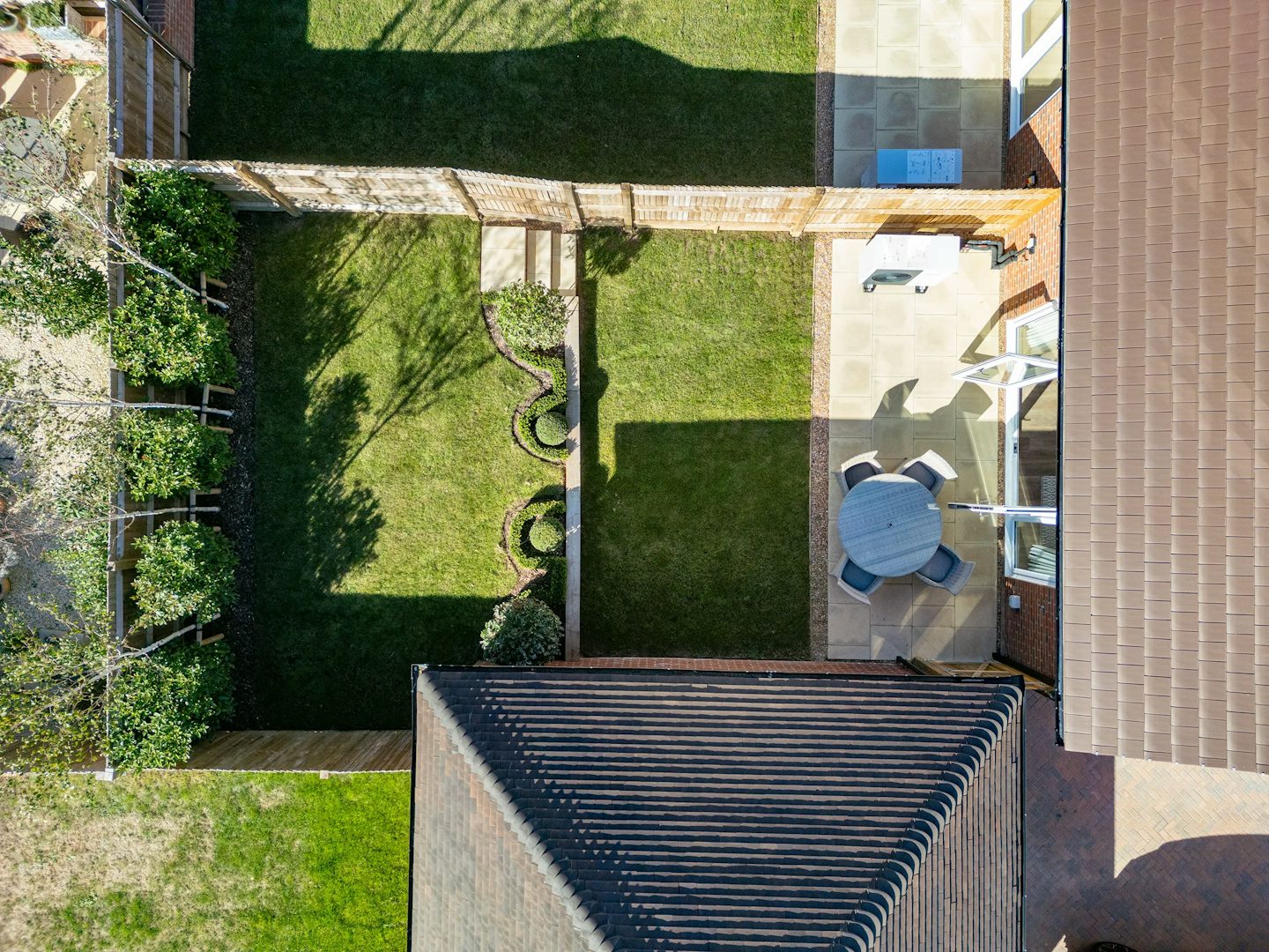 Aerial view of a private rear garden showing lawn areas, patio seating space, planting beds, and fenced boundaries.