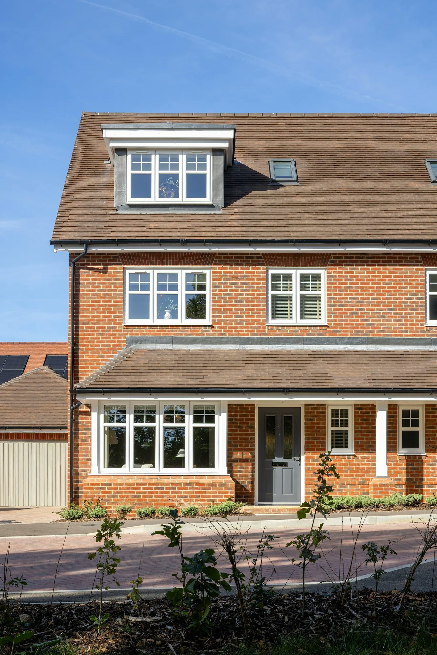 Exterior view of a three-storey brick-built home with dormer windows, covered entrance, and landscaped frontage.
