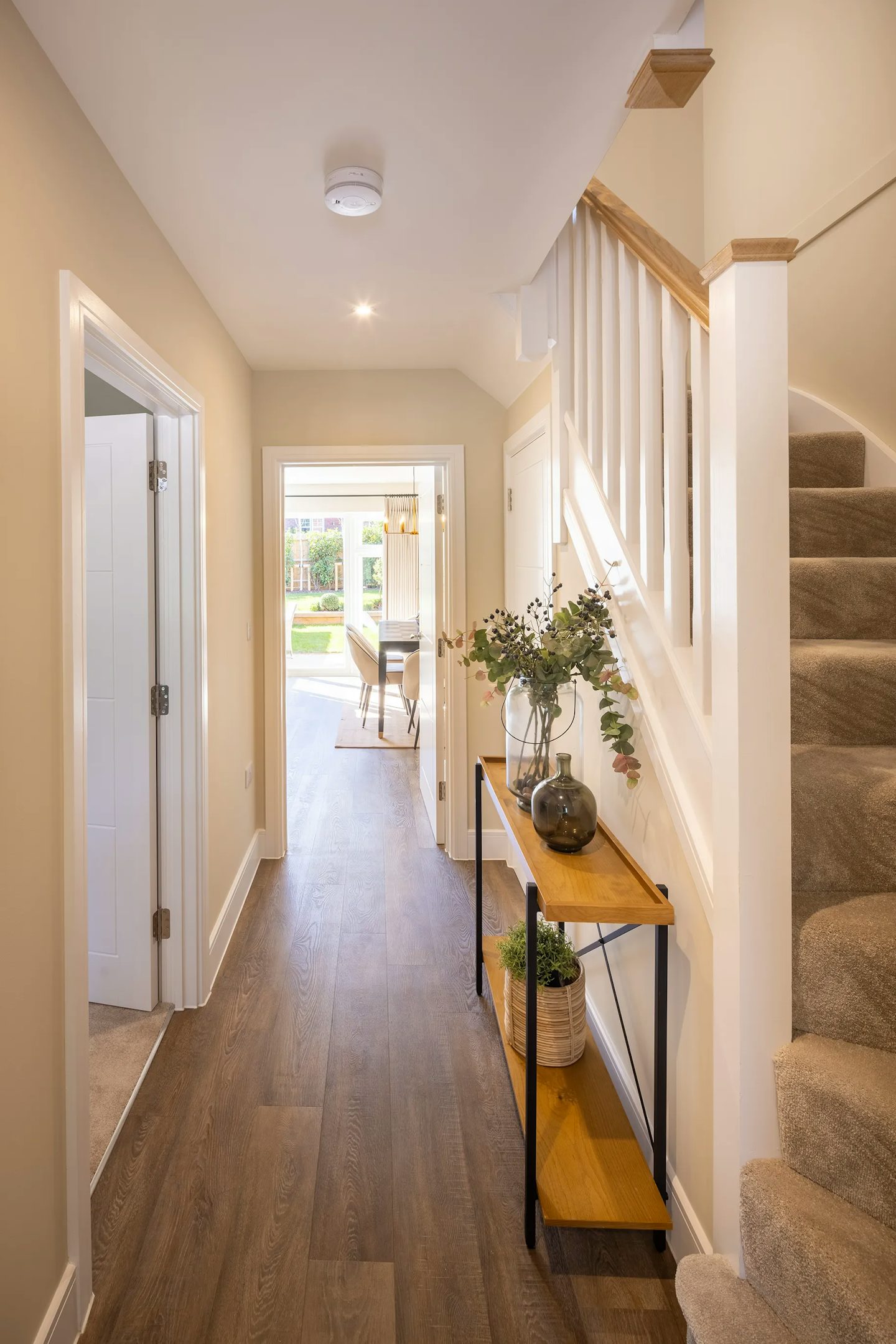 Bright entrance hallway with wood-effect flooring, staircase with white balustrade, console table, and views through to the dining area and garden.