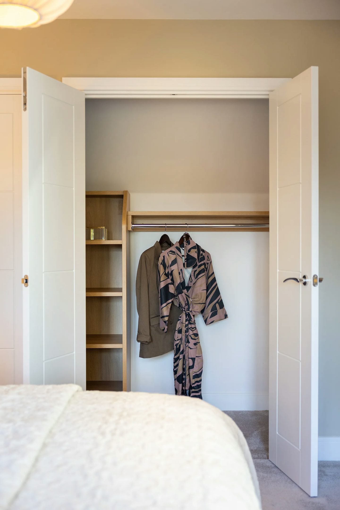 Built-in wardrobe with double doors, open shelving, hanging rail, and neatly displayed clothing.