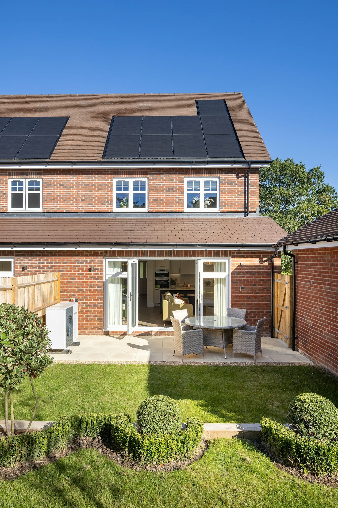 Landscaped rear garden with lawn, patio seating area, French doors to the home, and roof-mounted solar panels visible above.