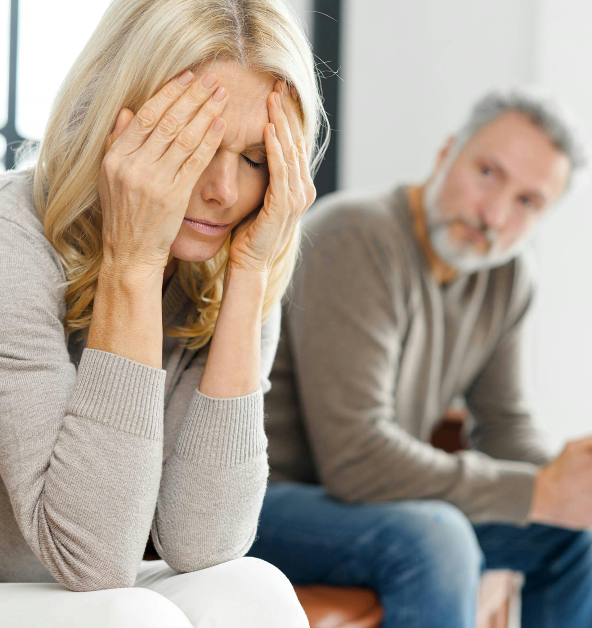 Woman holding her head in distress next to husband.