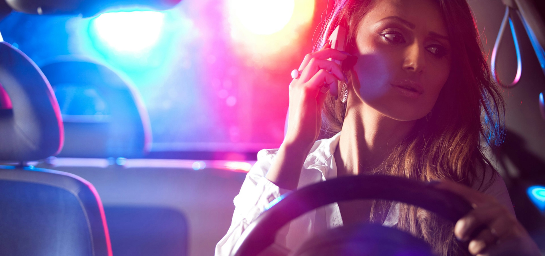 Woman on Phone in Car with Police Lights in Background - Traffic Violations Banner