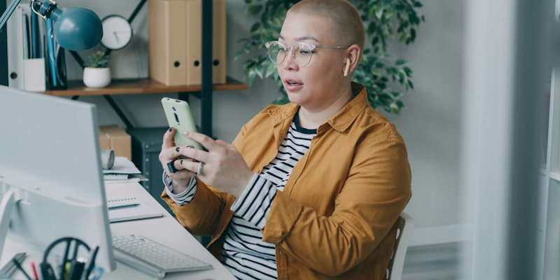 A woman sitting at a desk looking at a cell phone