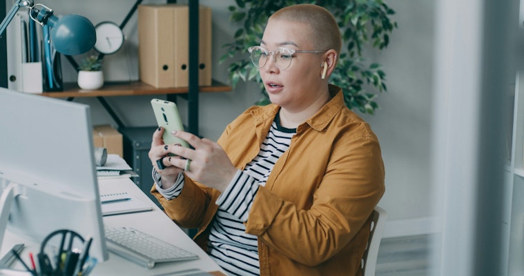 A woman sitting at a desk looking at a cell phone