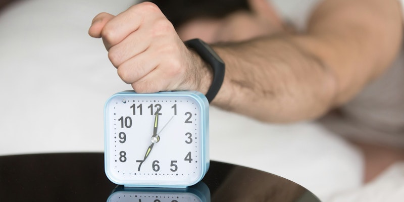 A man laying in bed with a clock on top of him