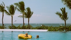 child on yellow pool float beside swimming woman