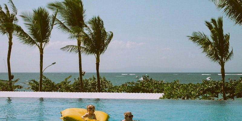 child on yellow pool float beside swimming woman