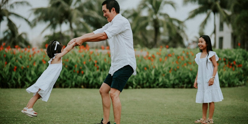 Father spinning his daughter while another watches