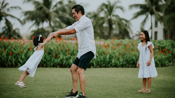 Father spinning his daughter while another watches