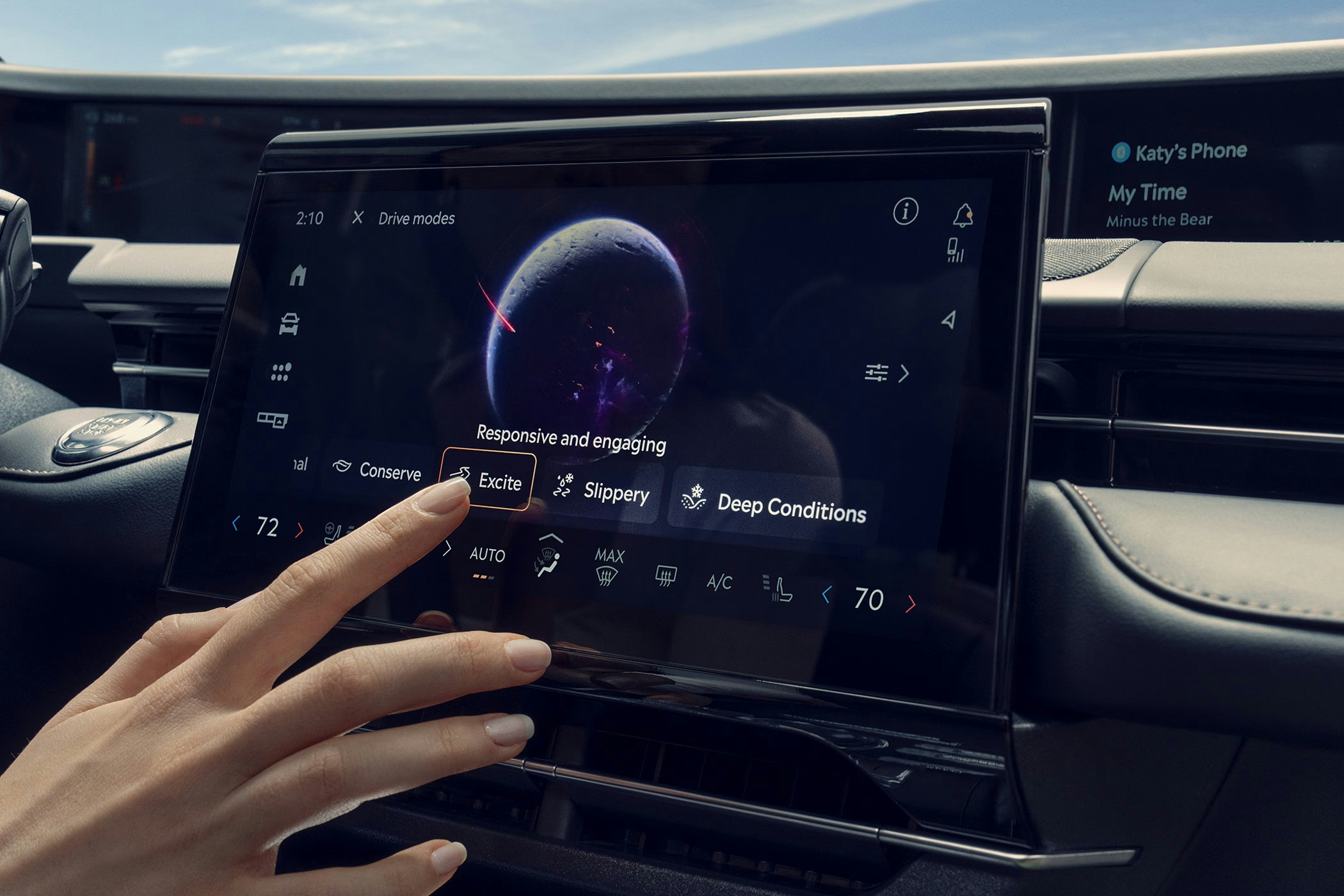 A hand touches a car’s touchscreen display, selecting the Excite driving mode. The screen shows various drive modes and climate controls, with a futuristic planet graphic in the background.