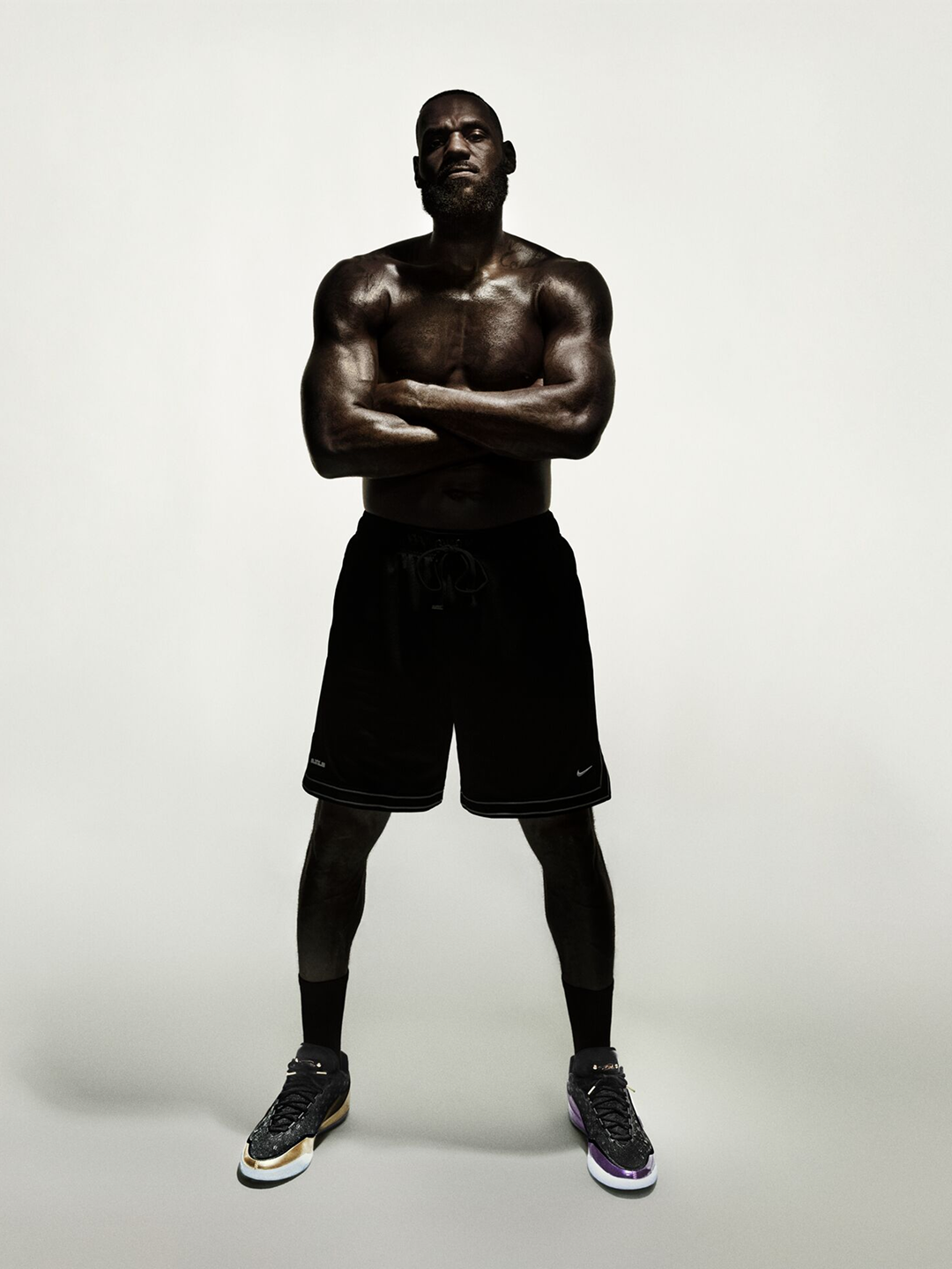 Studio portrait of LeBron James standing with arms crossed, wearing black shorts and LeBron XXIII shoes.