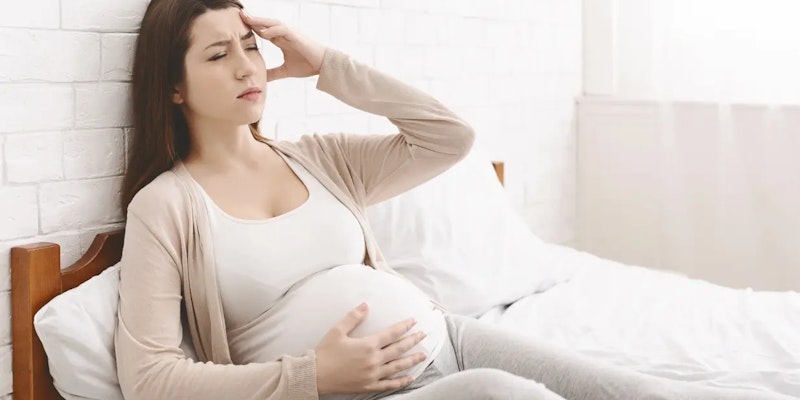 Mulher com a mão na barriga, sentido os sintomas da gravidez.
