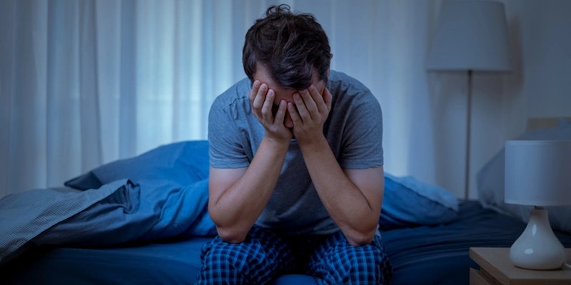 Imagem de uma pessoa com insônia, sentada em uma cama.