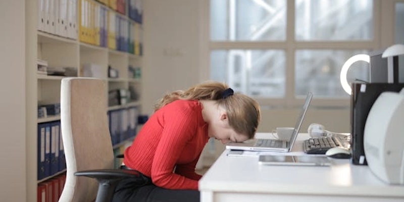 Imagem de mulher em mesa com computador, com sua cabeça apoiada, aparentando estar sob estresse prolongado.