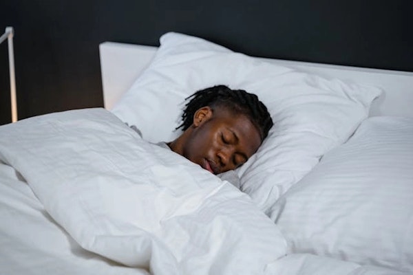 Imagem de um homem dormindo em uma cama com lençóis brancos.