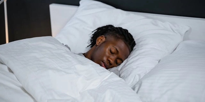 Imagem de um homem dormindo em uma cama com lençóis brancos.