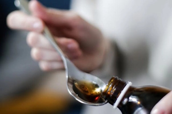 Pessoa servindo xarope em uma colher, representando medicamentos com clobutinol usados para tosse seca e a importância de consultar a bula antes do tratamento.