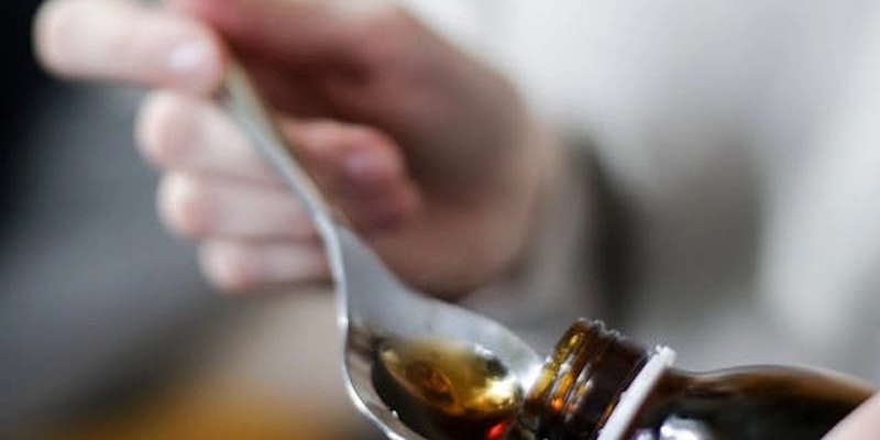 Pessoa servindo xarope em uma colher, representando medicamentos com clobutinol usados para tosse seca e a importância de consultar a bula antes do tratamento.