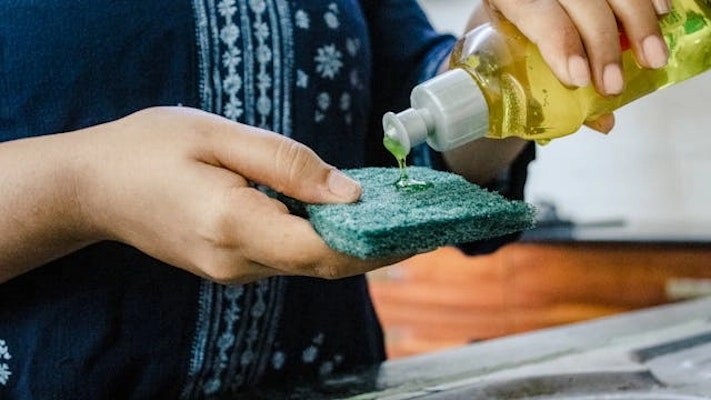 Pessoa aplicando lava-louças em uma esponja, em referência aos produtos Ypê com alerta da Anvisa, lotes afetados e risco de contaminação microbiológica.