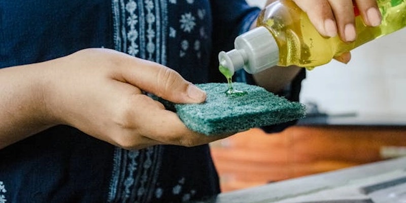 Pessoa aplicando lava-louças em uma esponja, em referência aos produtos Ypê com alerta da Anvisa, lotes afetados e risco de contaminação microbiológica.