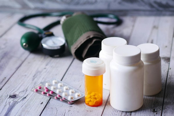 Frascos de medicamentos e aparelho de pressão arterial sobre mesa, ilustrando o uso de Indapamida no controle da pressão alta e retenção de líquidos.