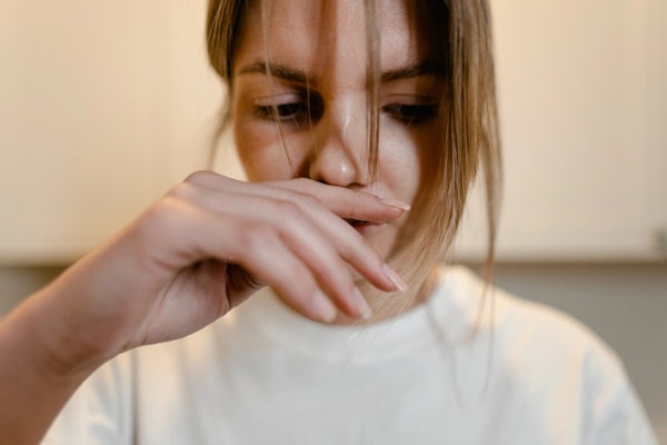 Mulher com expressão de enjoo cobrindo a boca com a mão, ilustrando sintomas tratados pelo Plasil, como náusea e vontade de vomitar.
