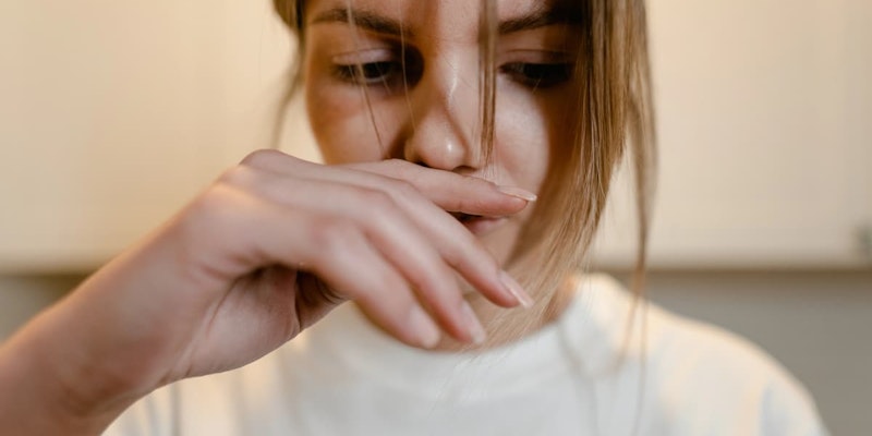 Mulher com expressão de enjoo cobrindo a boca com a mão, ilustrando sintomas tratados pelo Plasil, como náusea e vontade de vomitar.