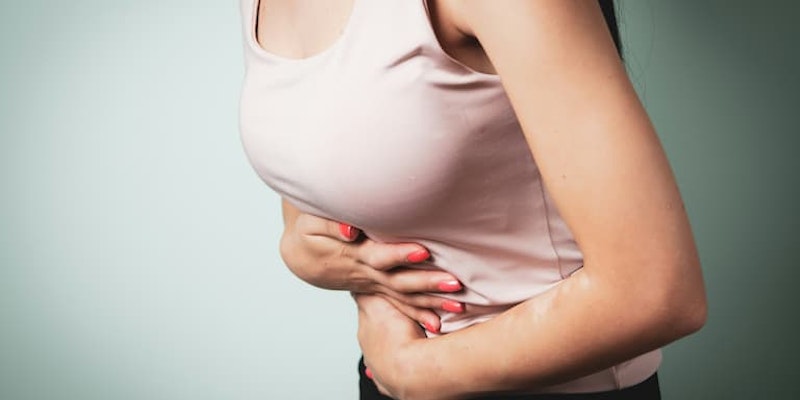 Pessoa segurando a região abdominal com expressão de desconforto com sintomas gastrointestinais como diarreia e desequilíbrio da flora intestinal, situações em que o Floratil pode ser utilizado.