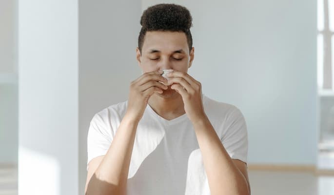 Homem segurando um lenço próximo ao nariz com sintomas de alergia, gripe ou resfriado.