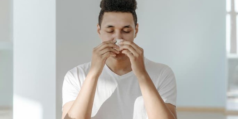 Homem segurando um lenço próximo ao nariz com sintomas de alergia, gripe ou resfriado.