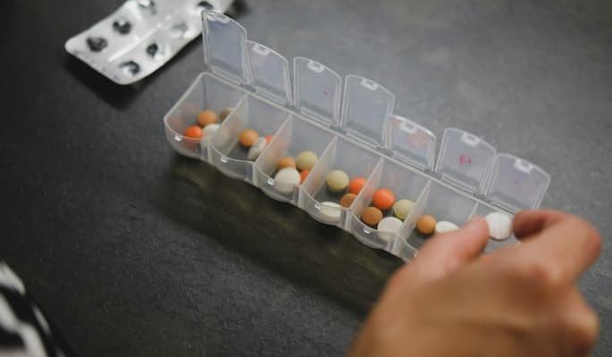Pessoa organizando comprimidos em uma caixa semanal de medicamentos para não esquecer de tomar o remédio.