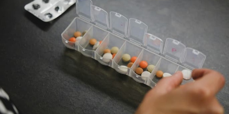 Pessoa organizando comprimidos em uma caixa semanal de medicamentos para não esquecer de tomar o remédio.