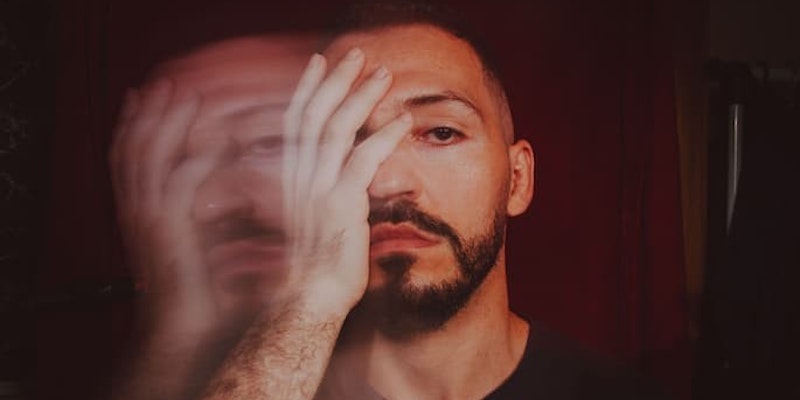 Homem com expressão séria e efeito visual de duplicação do rosto, com sintomas de transtornos mentais como esquizofrenia e do transtorno bipolar tratados com olanzapina.