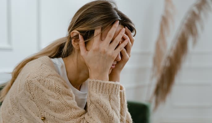 Mulher com as mãos no rosto em sinal de depressão, ansiedade ou desconforto emocional.