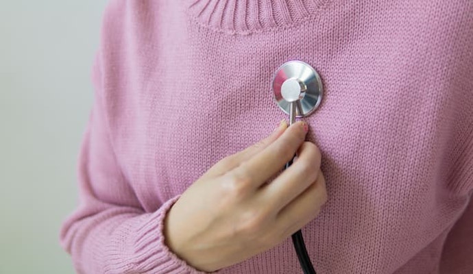 Pessoa com blusa rosa posicionando um estetoscópio sobre o peito para monitorar a saúde cardiovascular com hipertensão e doenças cardíacas tratadas com Selozok.